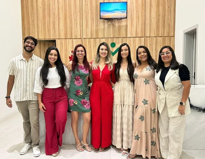 Sete integrantes da equipe da CSI reunidos e sorrindo no hall de recepção, diante do painel de madeira com o símbolo da clínica.